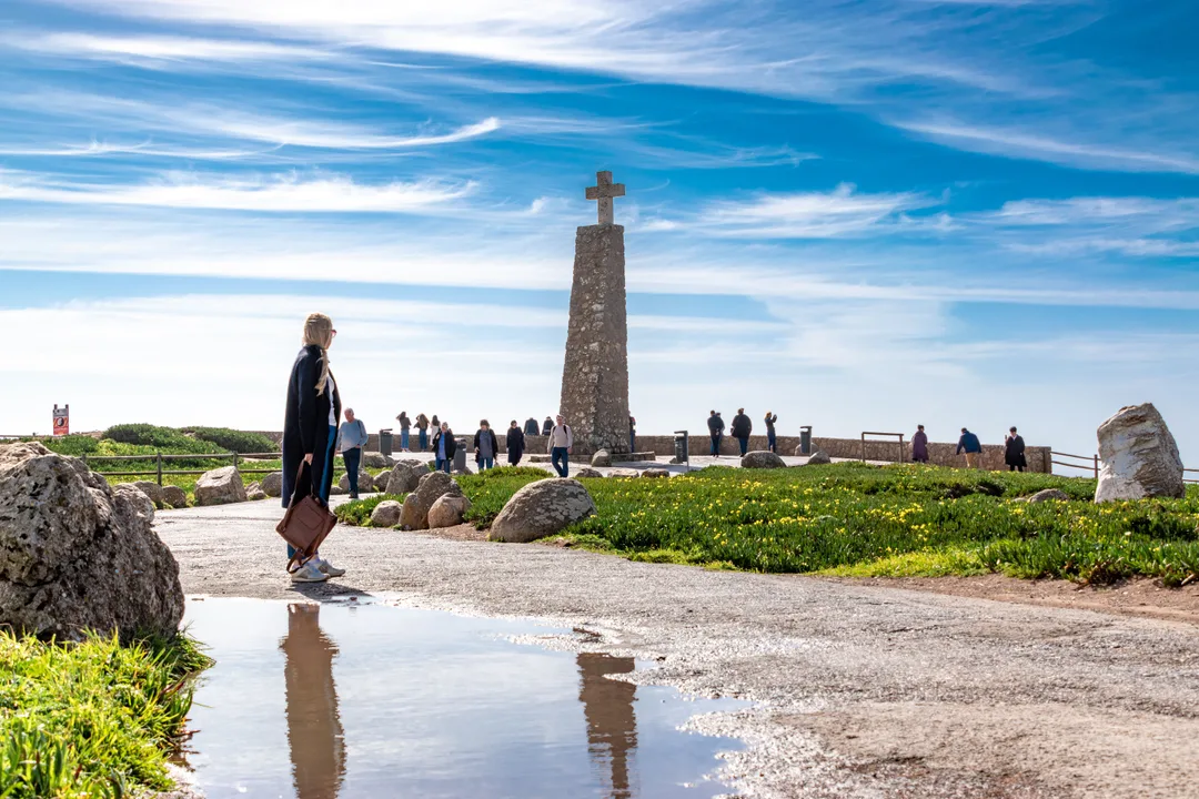 Stone cross monument at Cabo da Roca with visitors and ocean behind