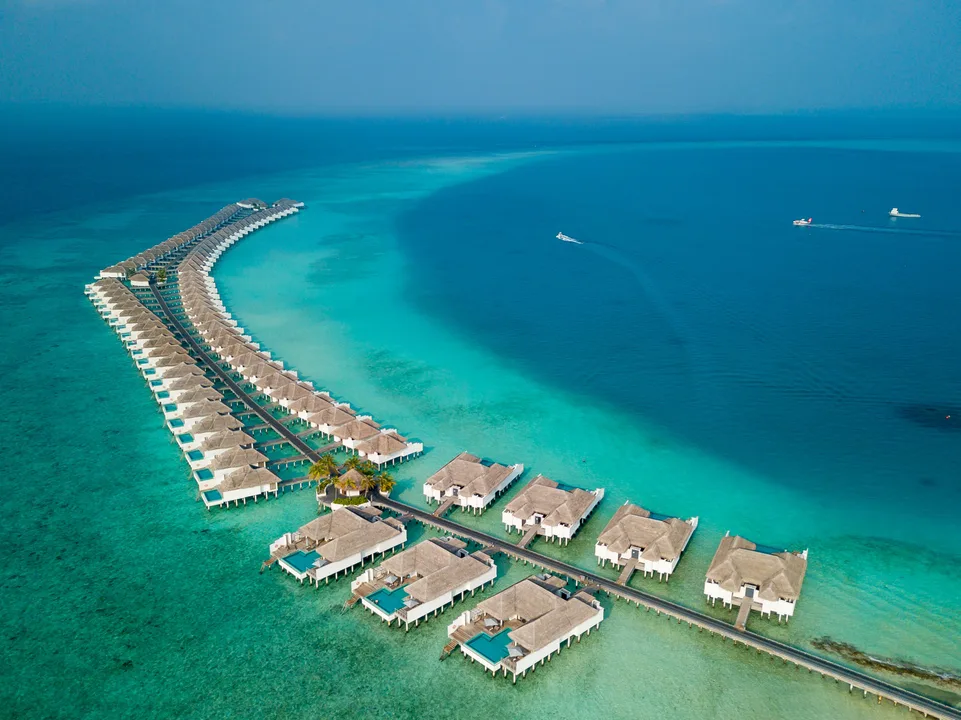 Aerial view of overwater villas curving across a turquoise Maldivian lagoon