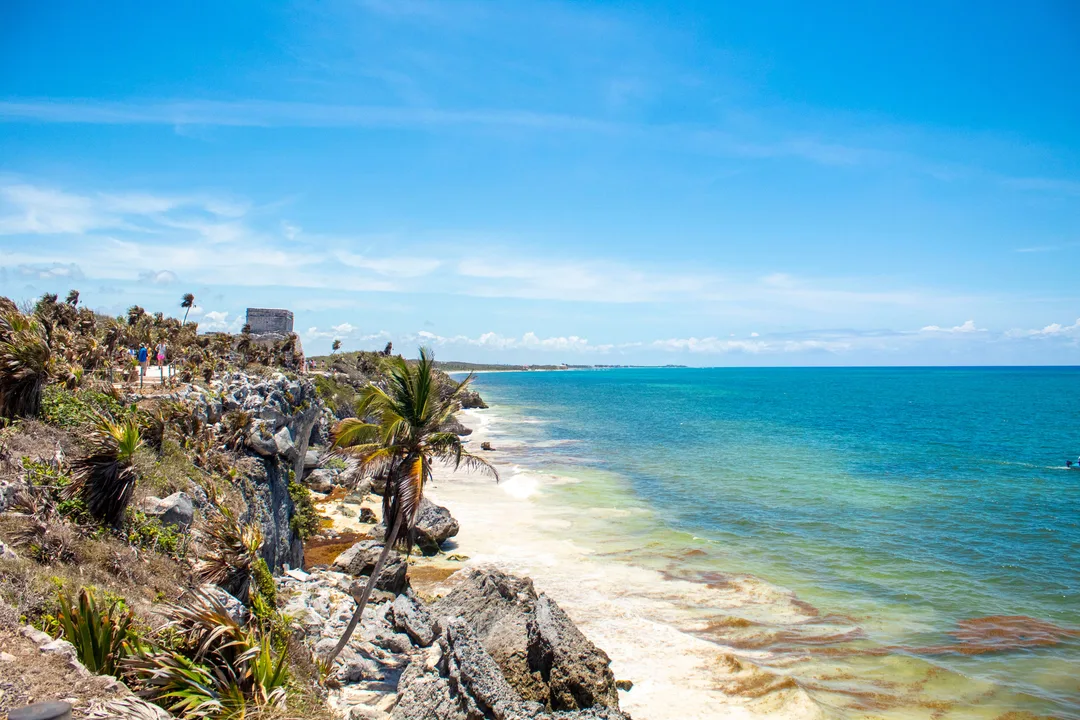 Tulum ruins standing on a rocky cliff above a white sand Caribbean beach