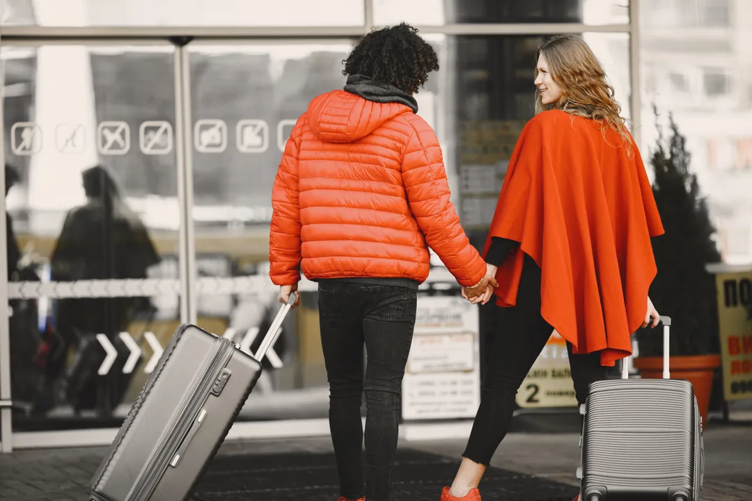 A couple pulling suitcases through a bright airport terminal before their honeymoon flight